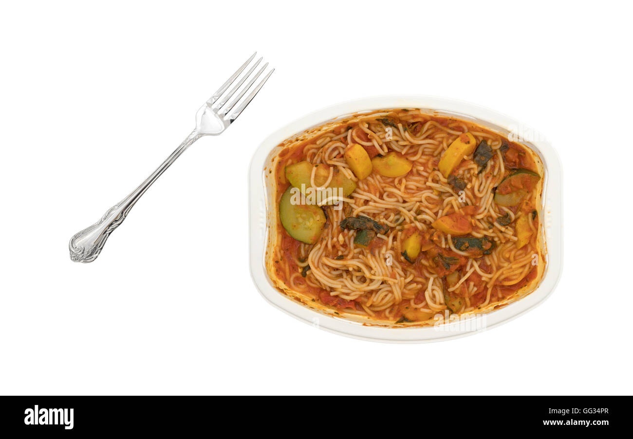 A cooked TV dinner of angel hair pasta with zucchini and spinach with a fork to the side in a microwaveable tray on a white back Stock Photo