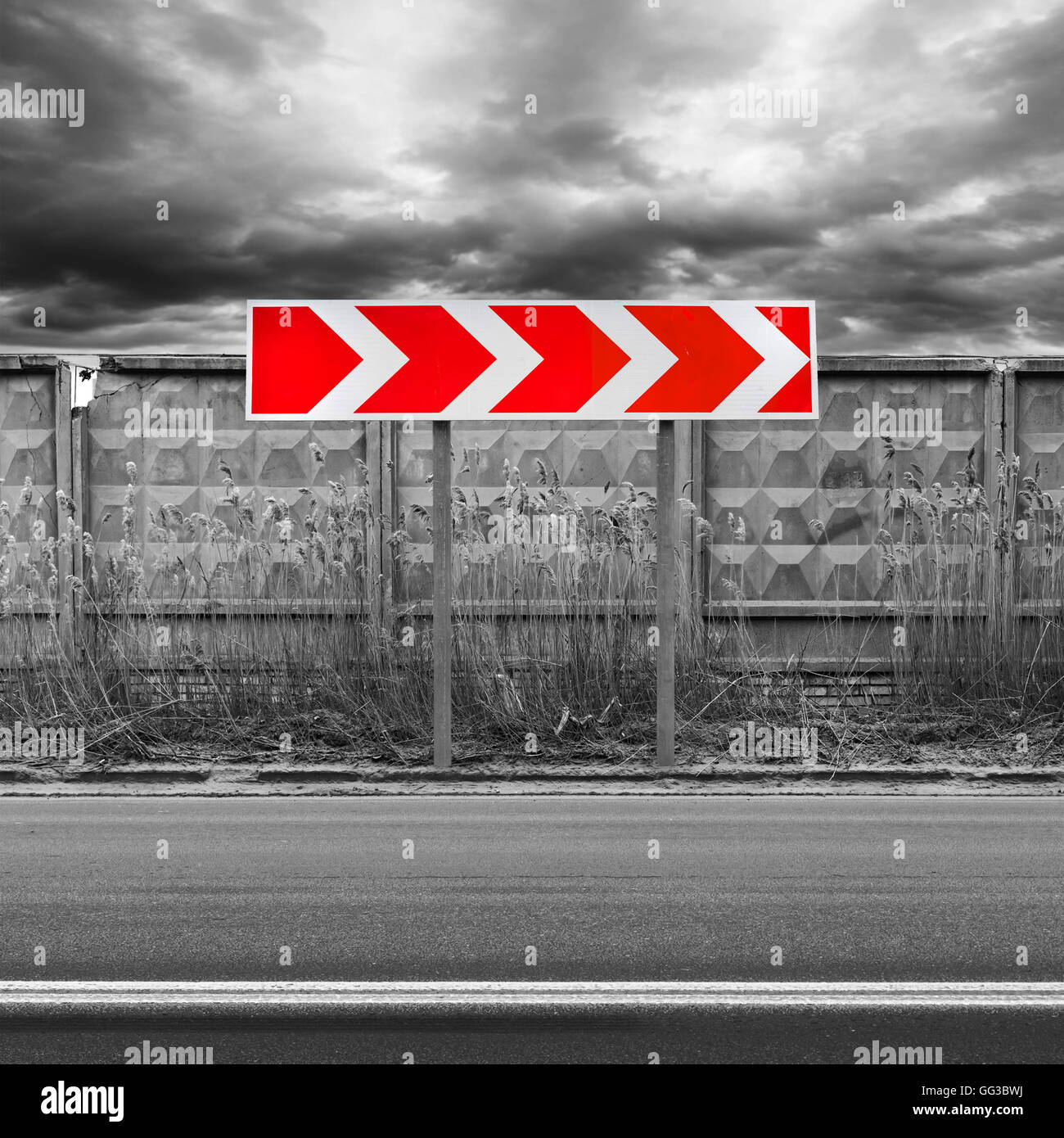 Red and white dangerous turn road sign stands near dark urban roadside with concrete fence Stock Photo