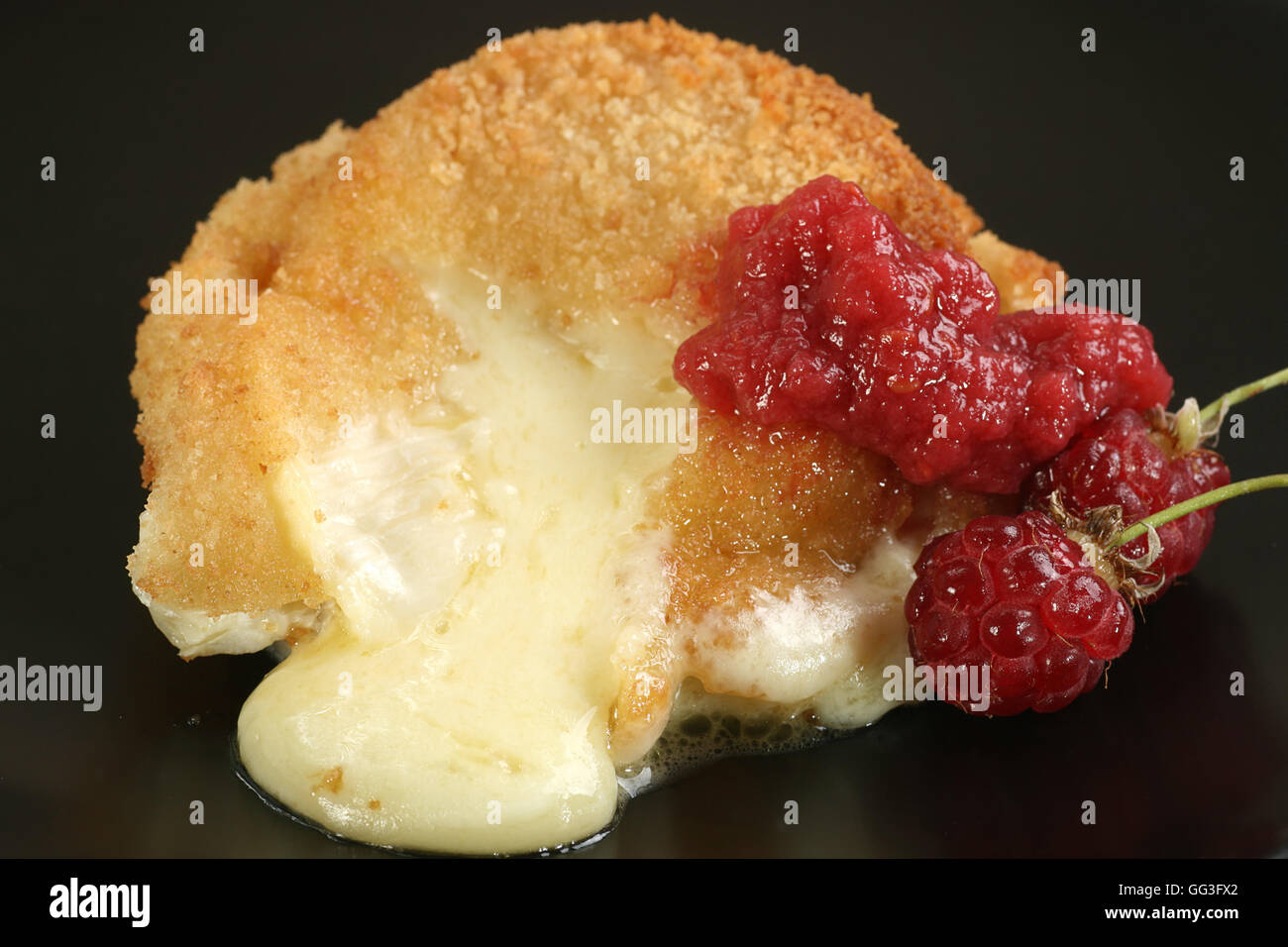 close up of baked and breaded camembert cheese with raspberry coulis