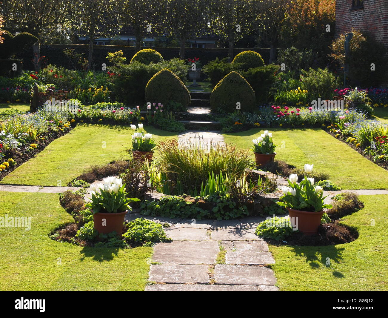 Ornamental pond in Chenies sunken garden backlit by sun in early spring with tulips, plant tubs