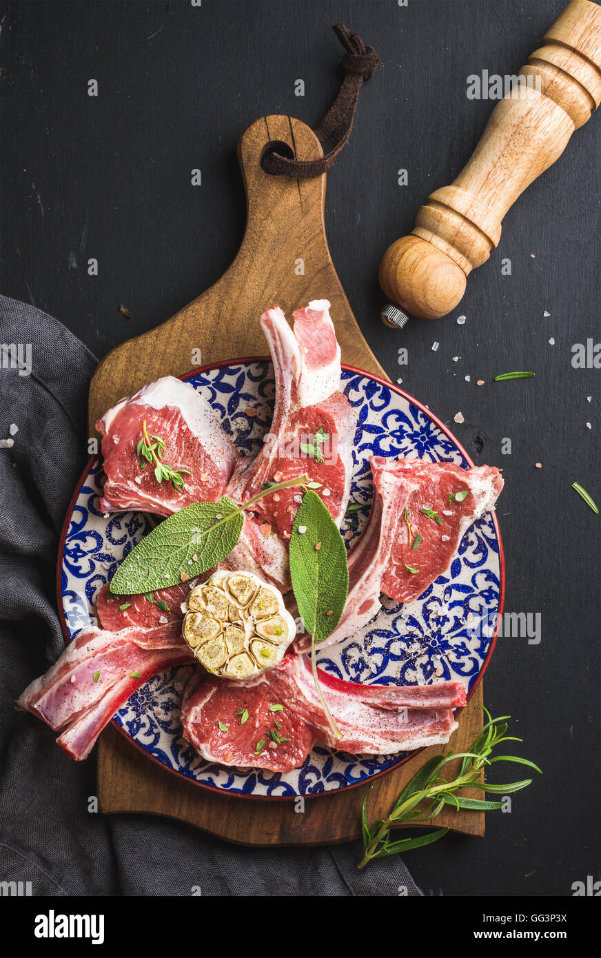 Raw uncooked lamb chops with herbs and spices on wooden board over dark
