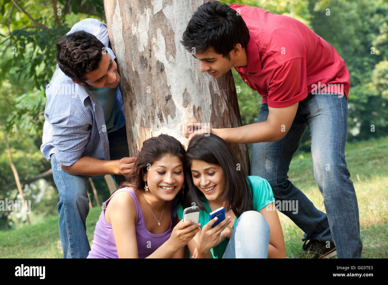 Young women sharing messages while men peeking from behind in lawn Stock Photo