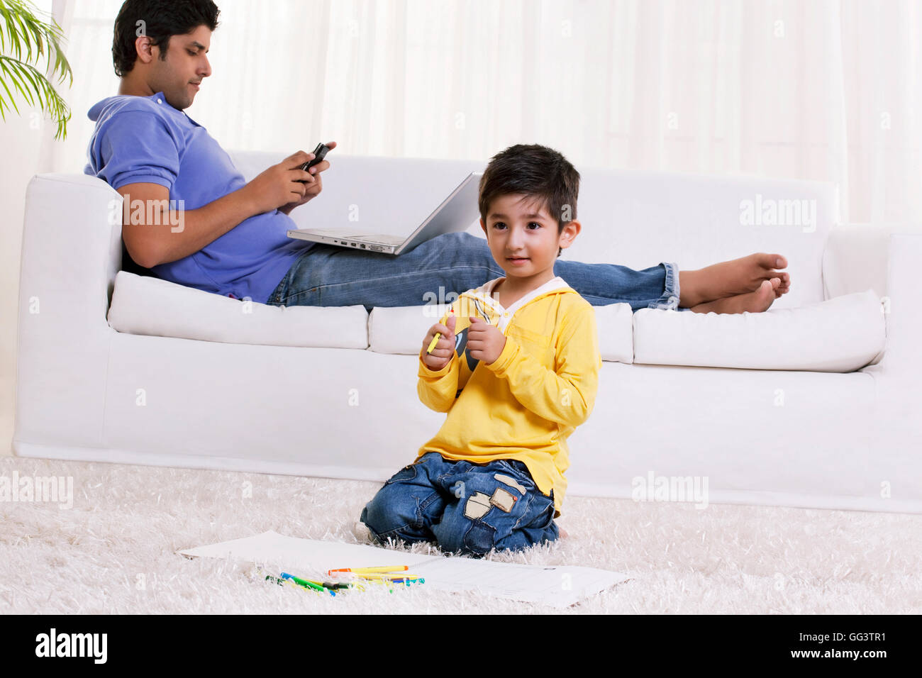 Boy holding felt tip pen with father using cell phone in the background Stock Photo
