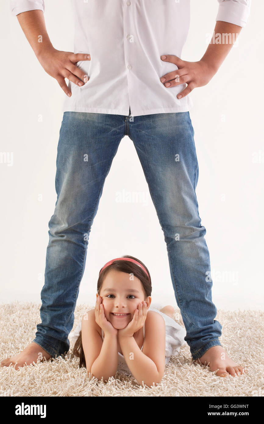 Portrait of cute girl lying between father's legs on rug Stock Photo
