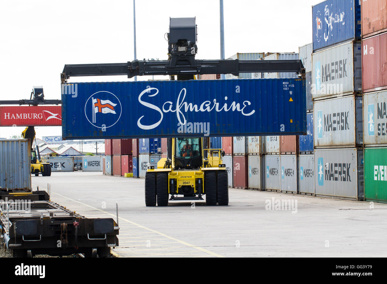 A heavy lifting machine unloading and loading cargo and shipping containers onto goods trains in a rail port or freight yard. Stock Photo