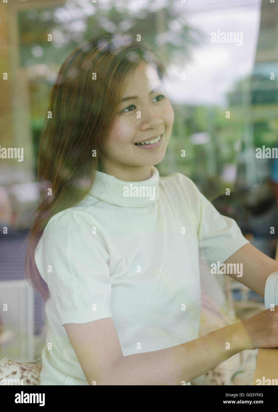 Beautiful asian woman sitting behind the window in cafe and reading a ...