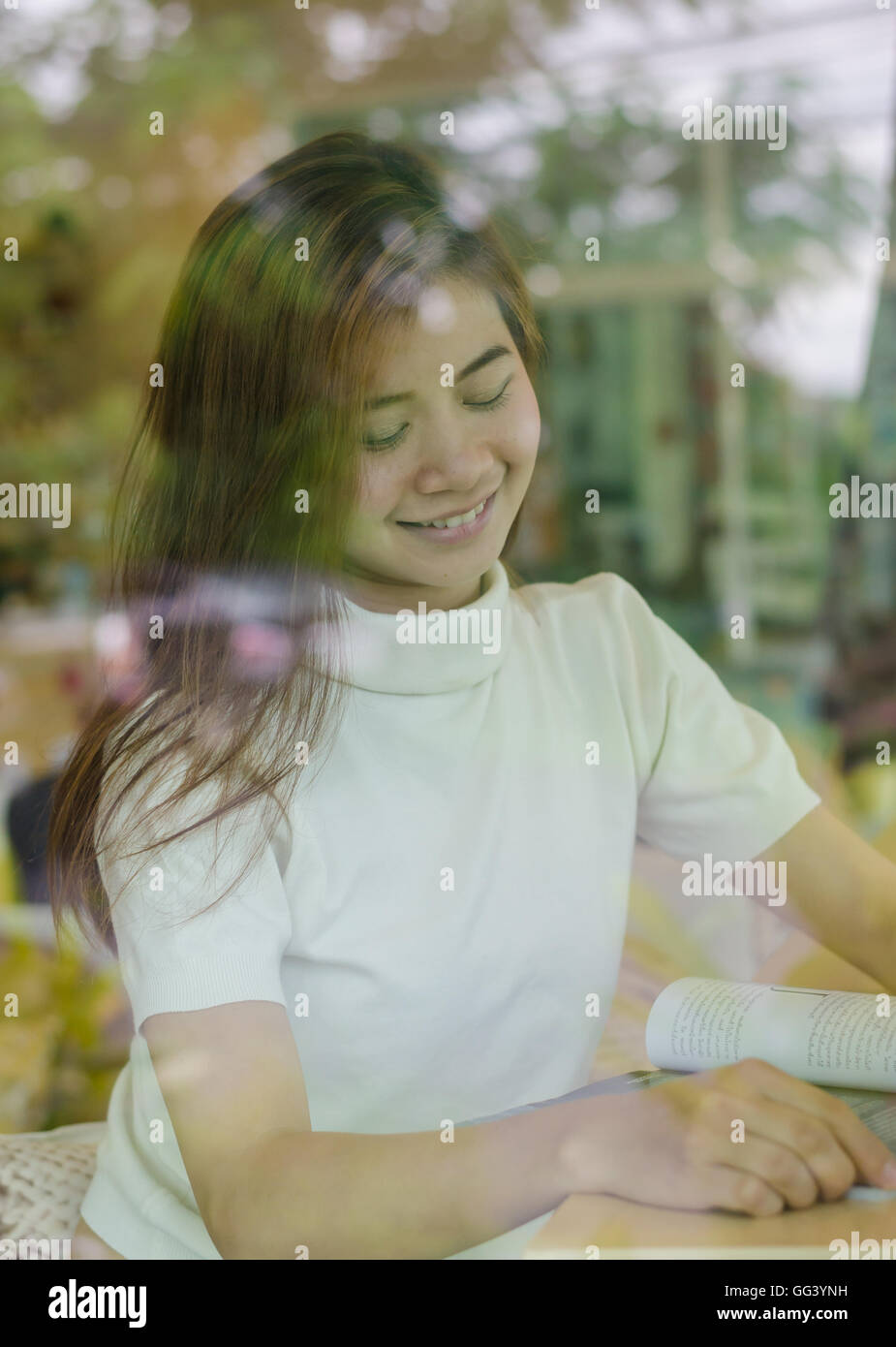 Beautiful asian woman sitting behind the window in cafe and reading a ...