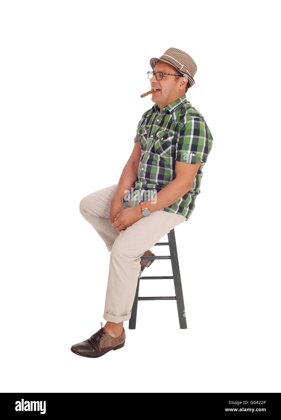 A middle age Hispanic man sitting on a chair and smoking his big cigar, wearing a beige hat, isolated for white background. Stock Photo