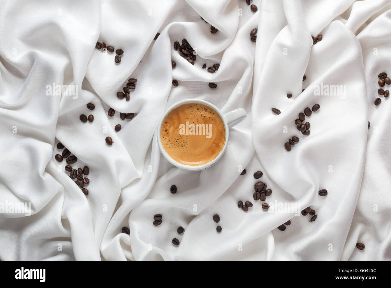 Coffee cup on a white silk fabric. Espresso and scattered beans. Top view. Stock Photo
