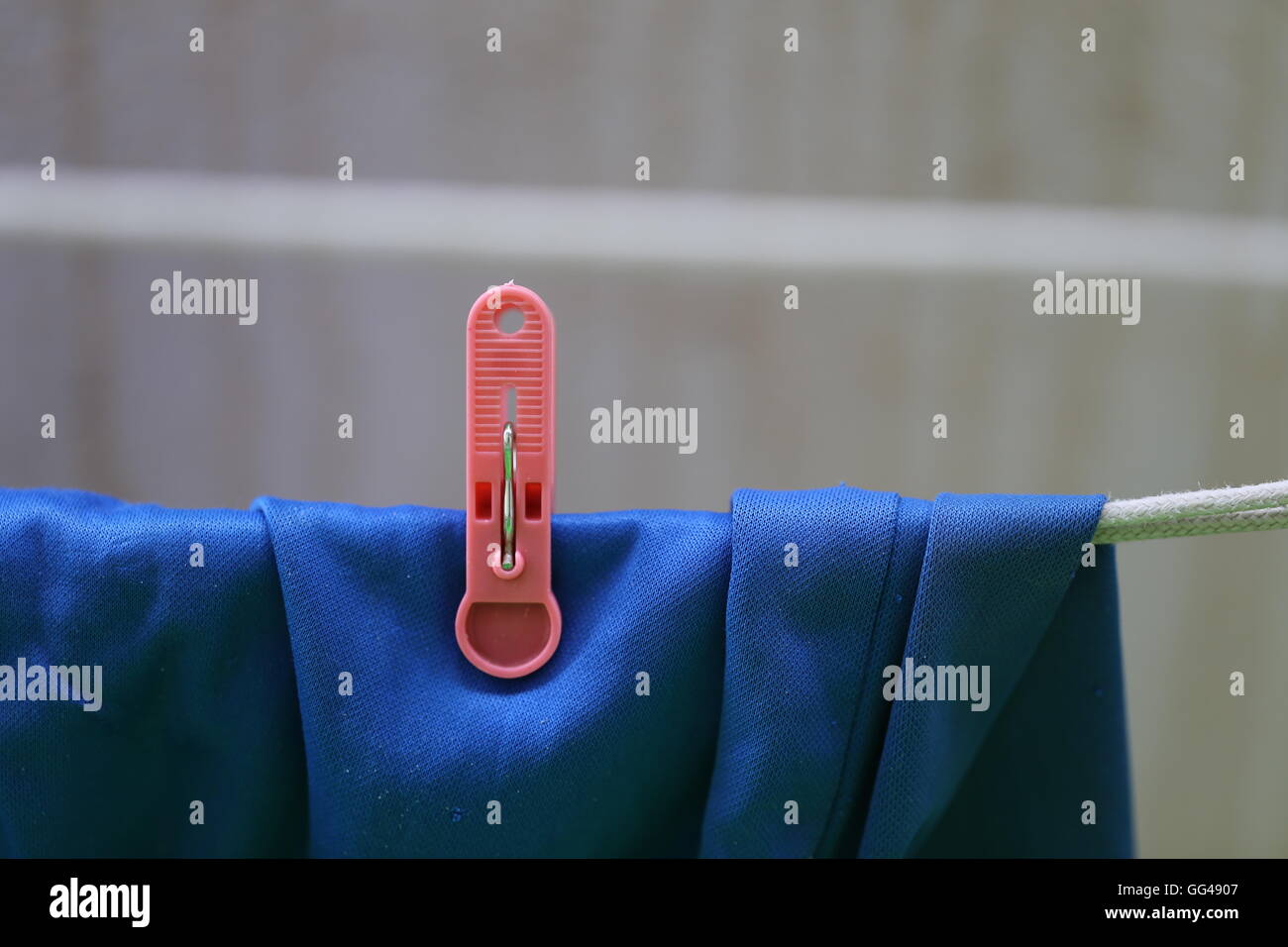 Blue Laundry Drying. Blue Shorts hanging on a clothes line with single red clothespin, plastic laundry stick. Sun drying  - green housekeeping. Stock Photo