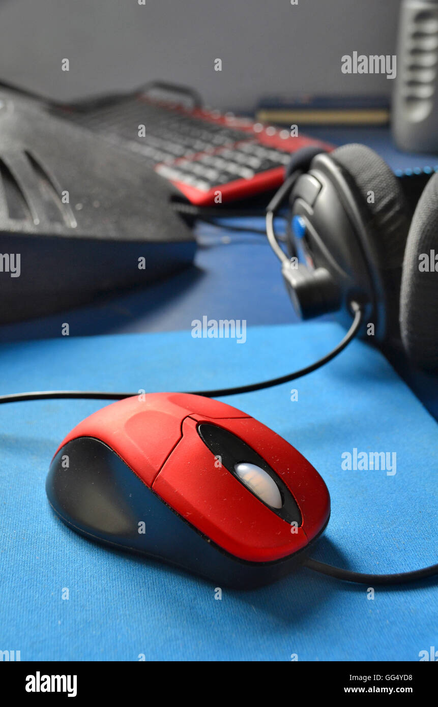 red scroll mouse and mat, computer headphones, and keyboard sit on a blue topped office desk. Stock Photo