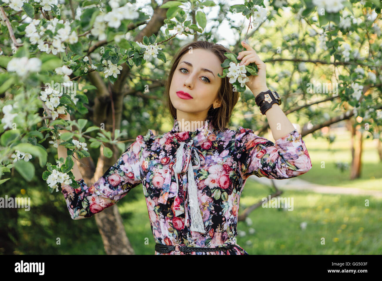 Beautiful young woman in dress standing near the blooming apple tree ...