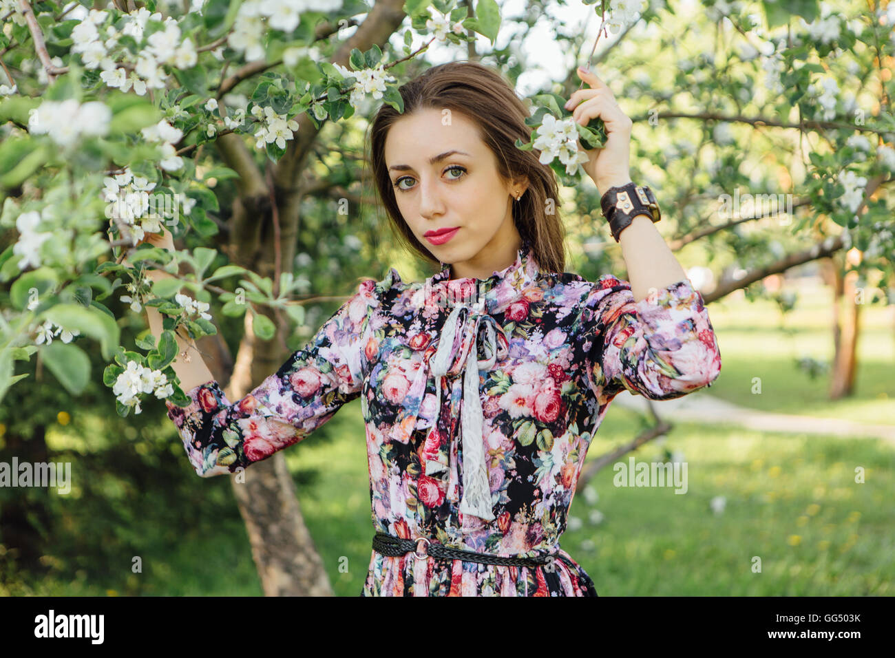 Beautiful young woman in dress standing near the blooming apple tree ...
