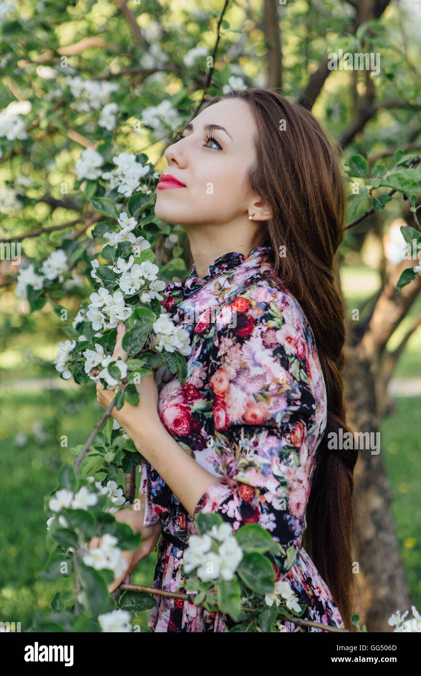 Beautiful young woman in dress standing near the blooming apple tree ...