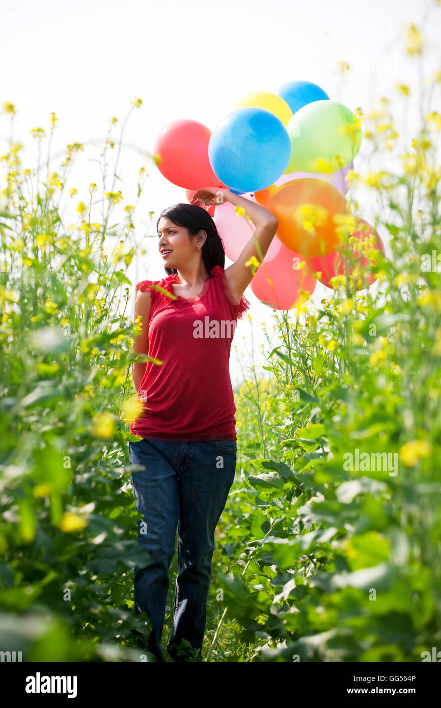 Young woman with balloons walking in a field Stock Photo