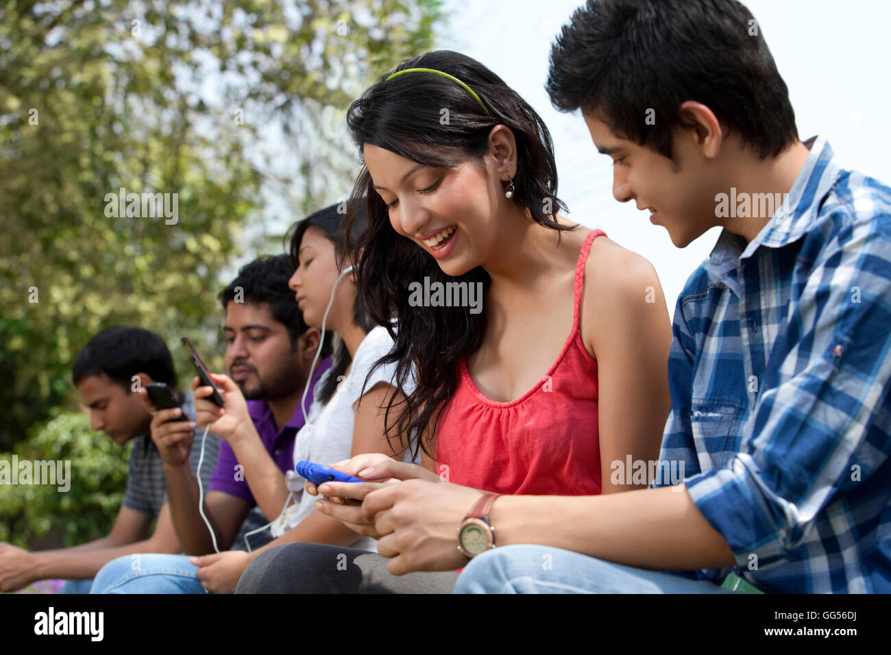 Young friends using cell phone with people in the background Stock Photo