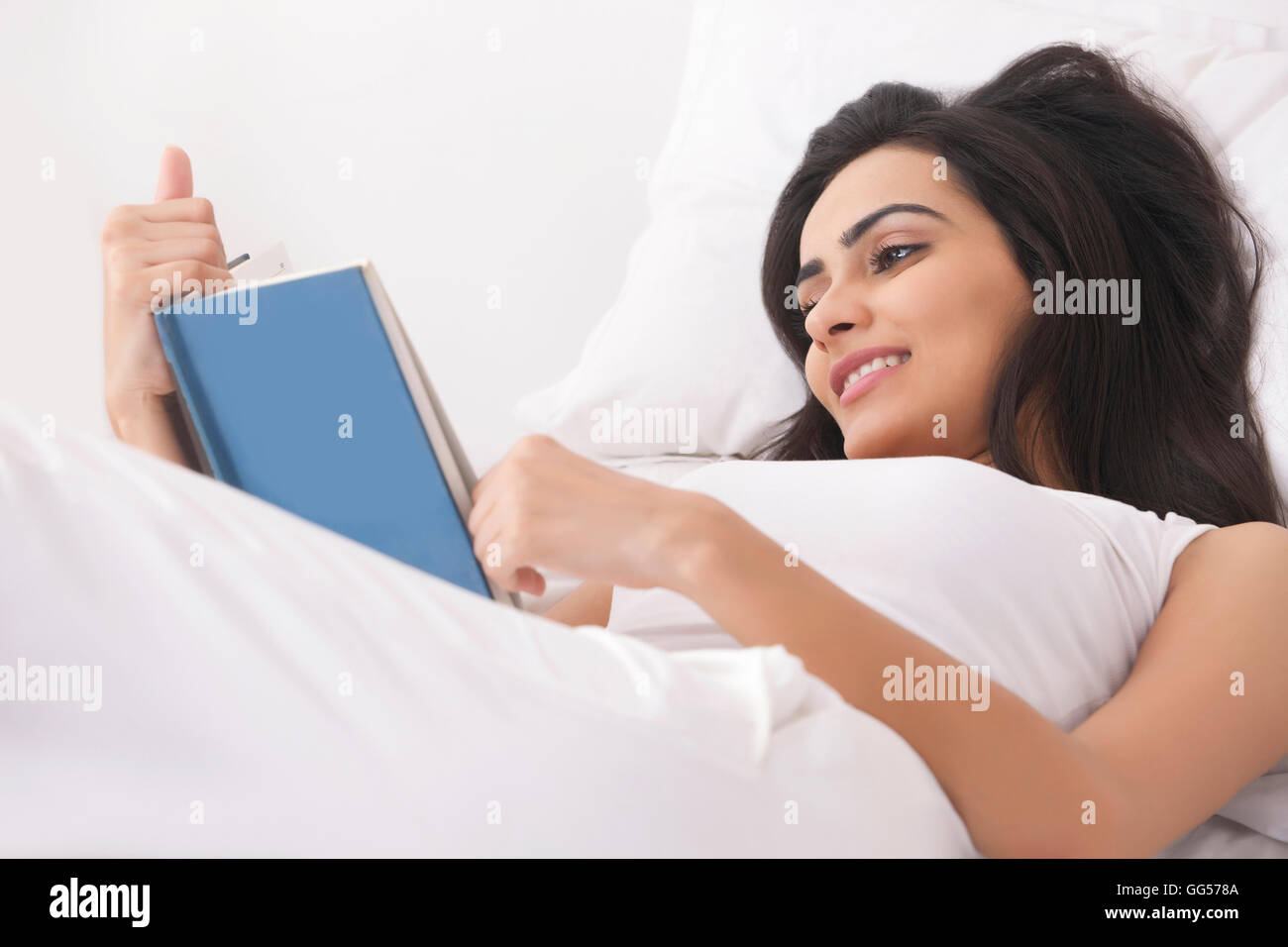 Beautiful young woman reading book in bed Stock Photo