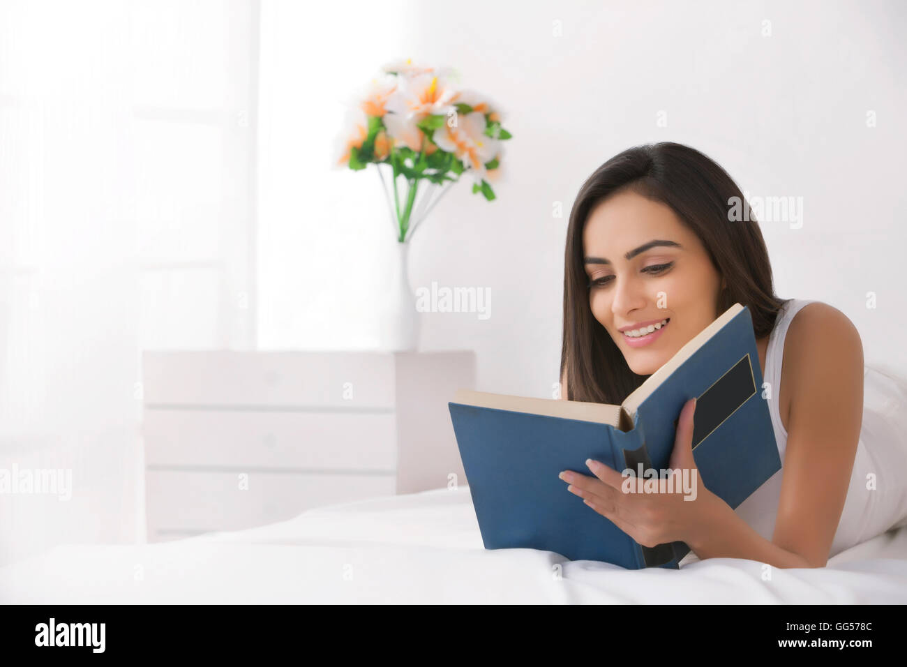 Beautiful young Indian woman reading book in bed Stock Photo