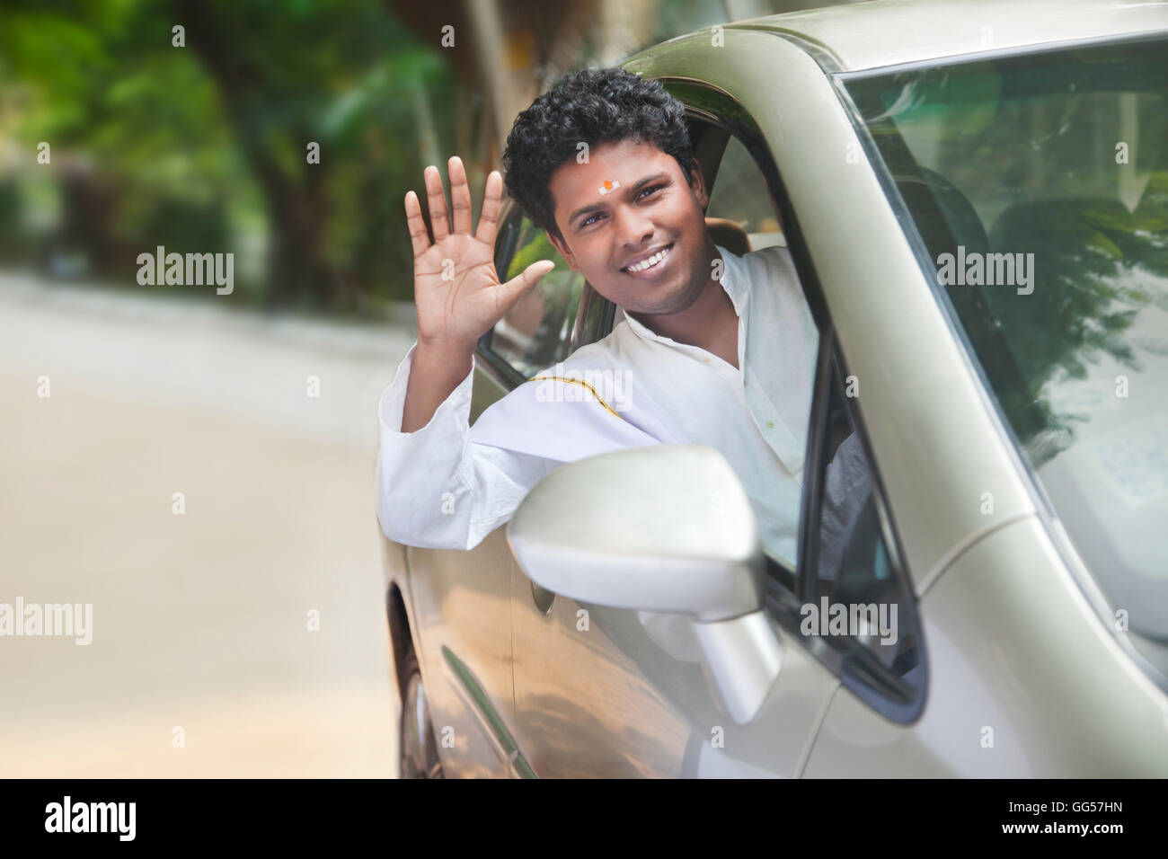 Portrait of smiling South Indian man waving out of car window Stock Photo