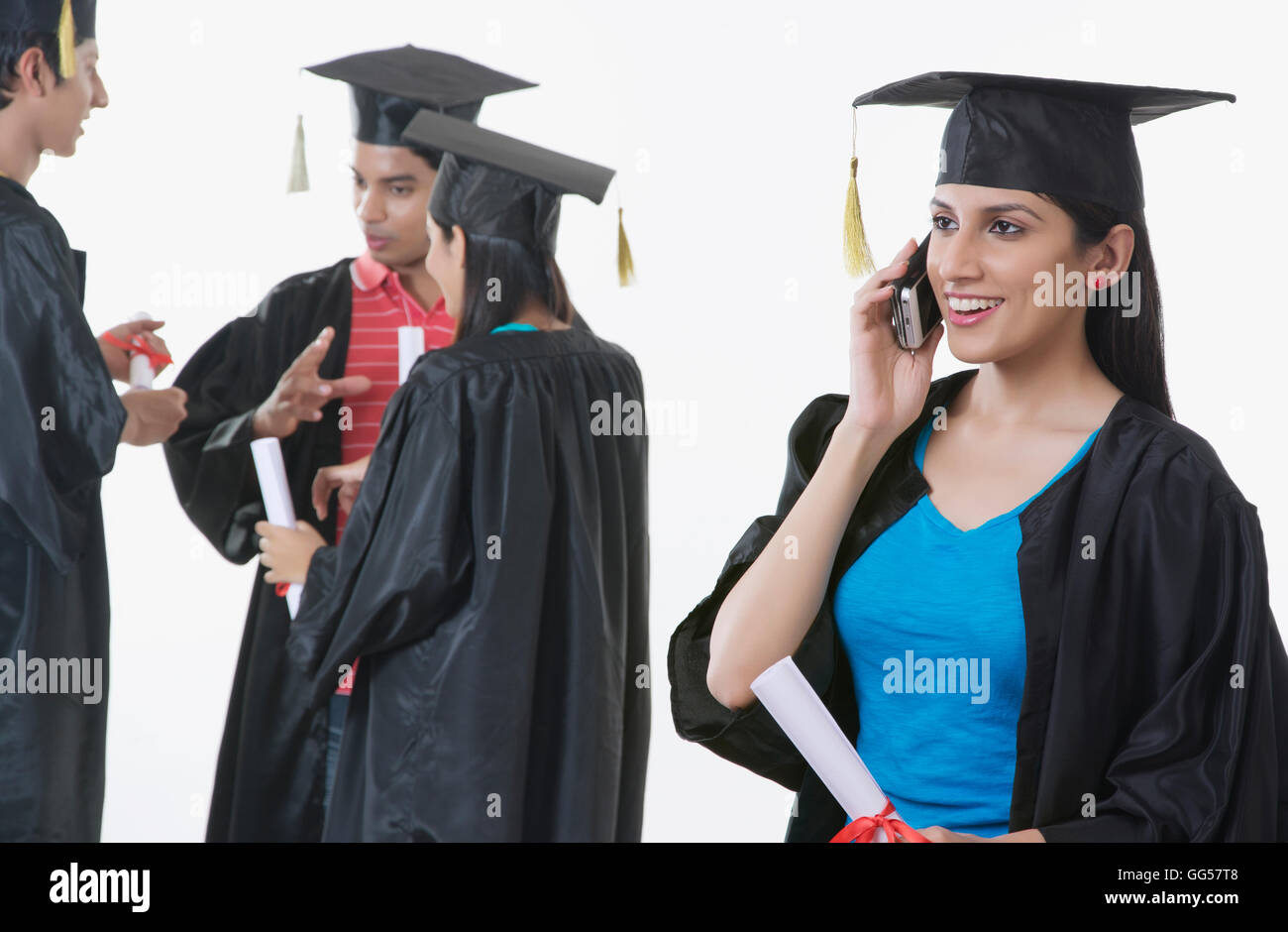 Smiling graduate student answering mobile phone with friends discussing against white background Stock Photo