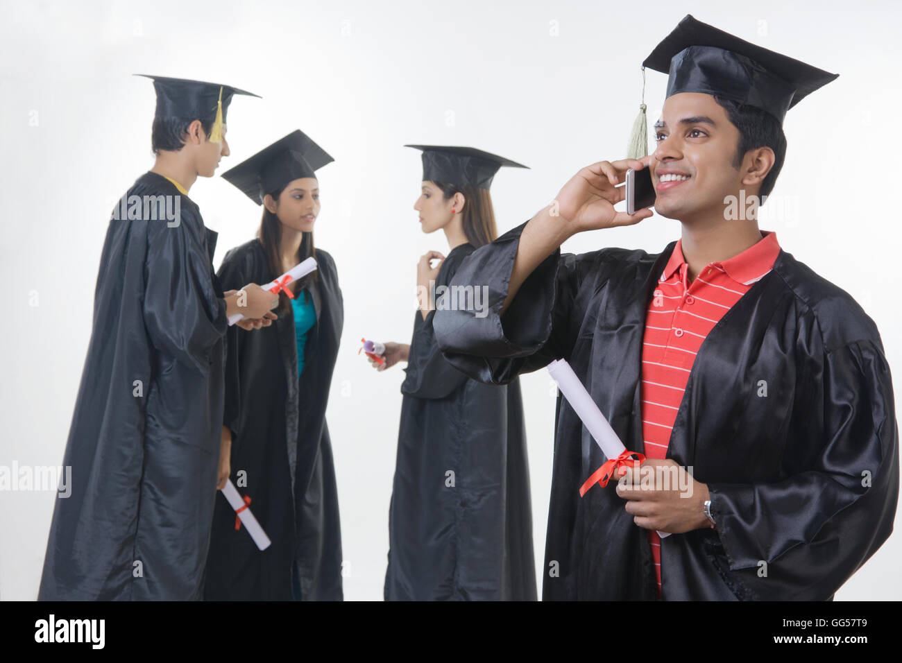 Happy graduate student answering smart phone with friends discussing against white background Stock Photo