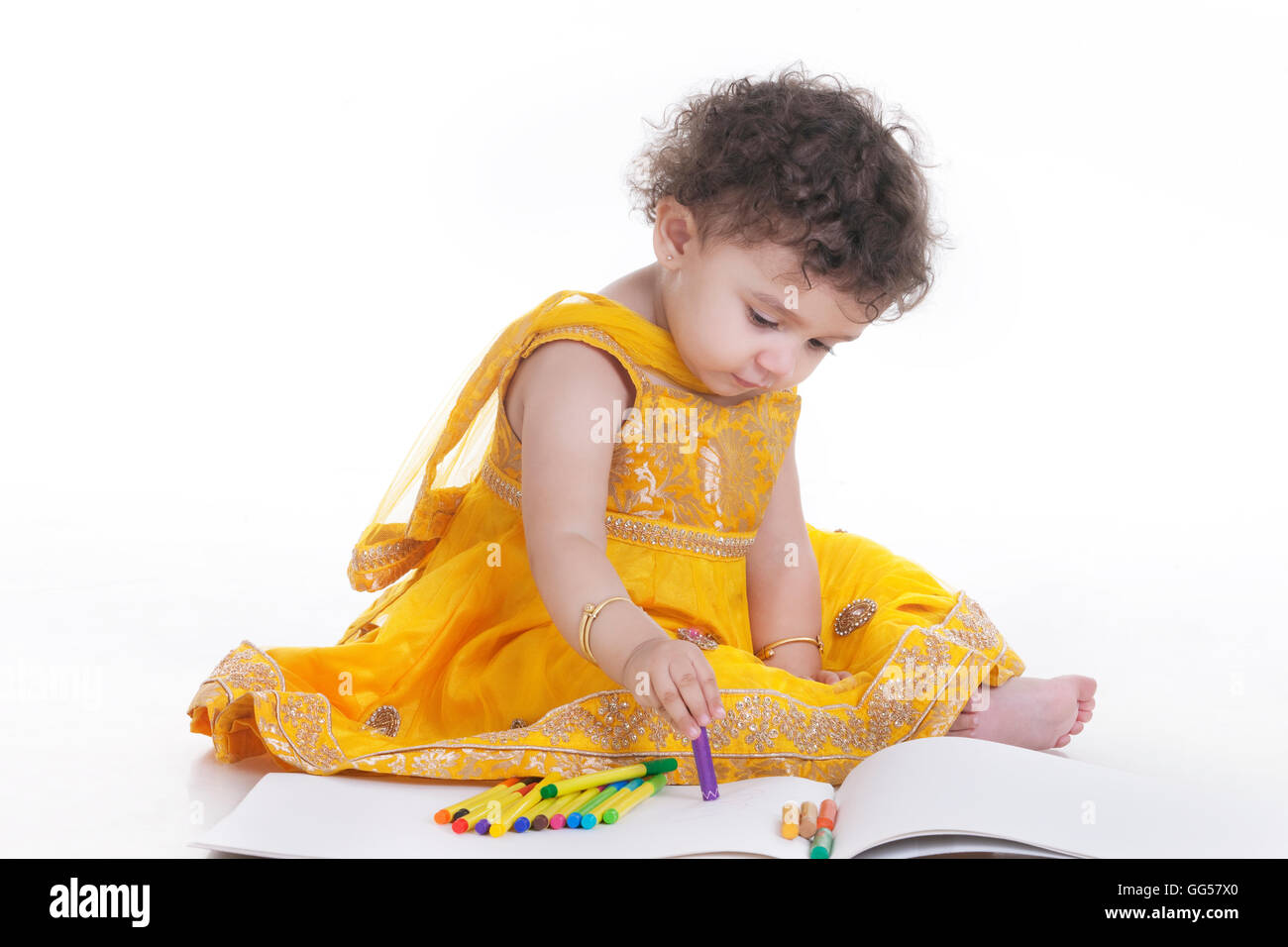 Full length of cute girl wearing salwar kameez drawing in book against white background Stock Photo