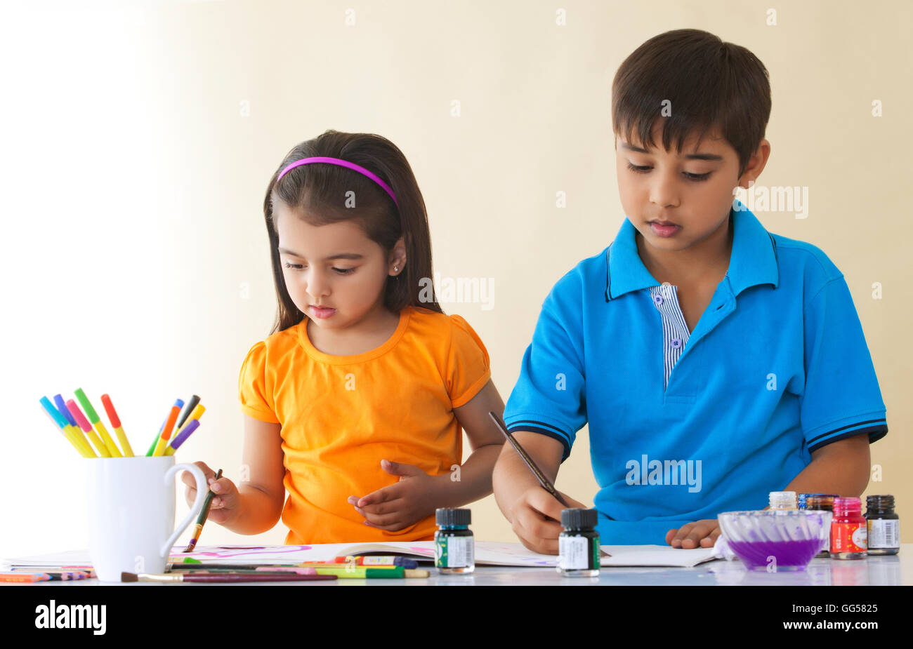 Siblings painting at table against colored background Stock Photo