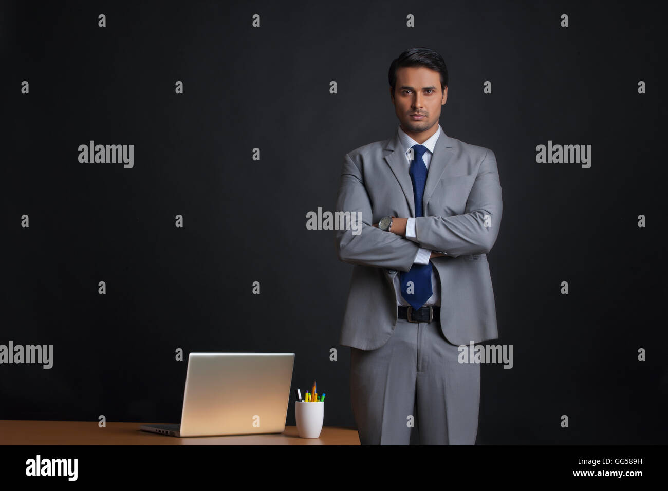 Portrait of young businessman standing arms crossed at office desk ...