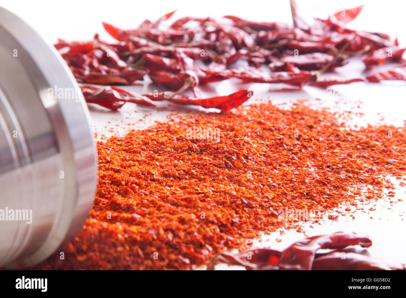 Chili powder and red chili peppers spread over white background Stock