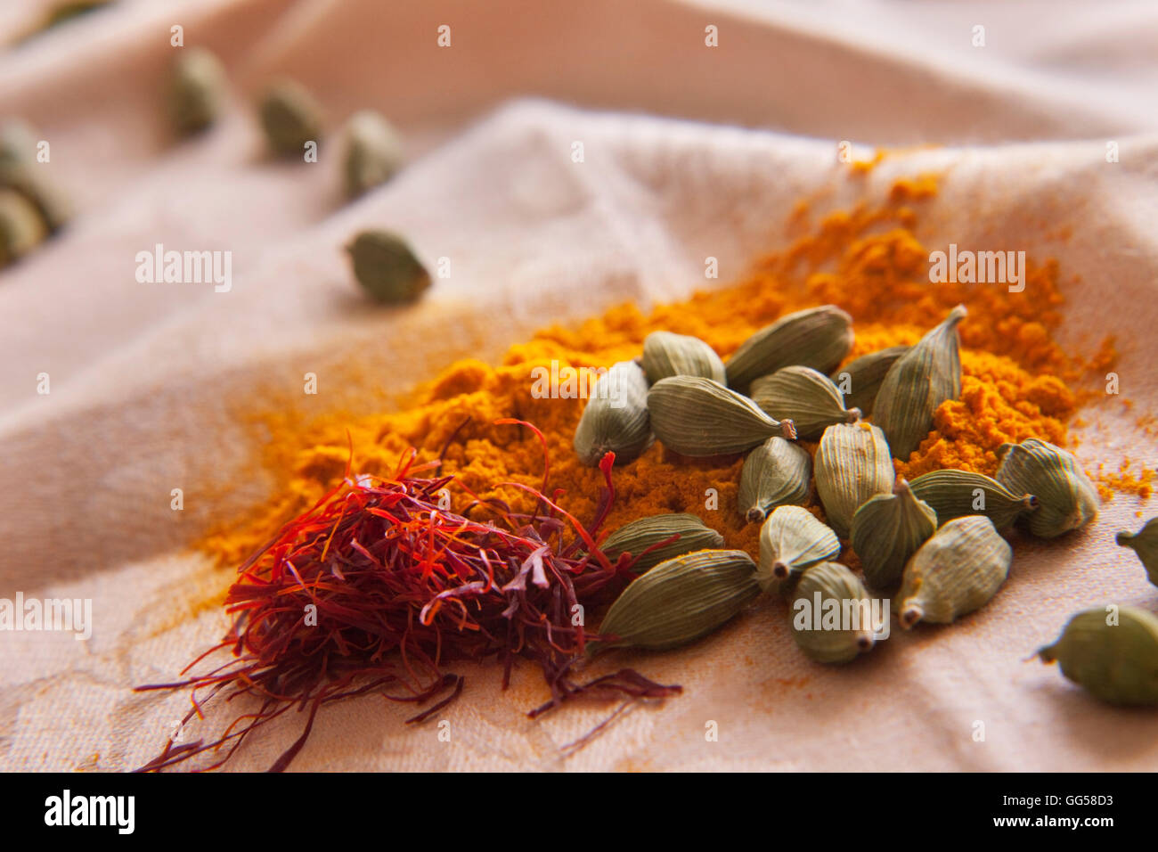 Green cardamom pods, saffron and turmeric powder on cloth Stock Photo