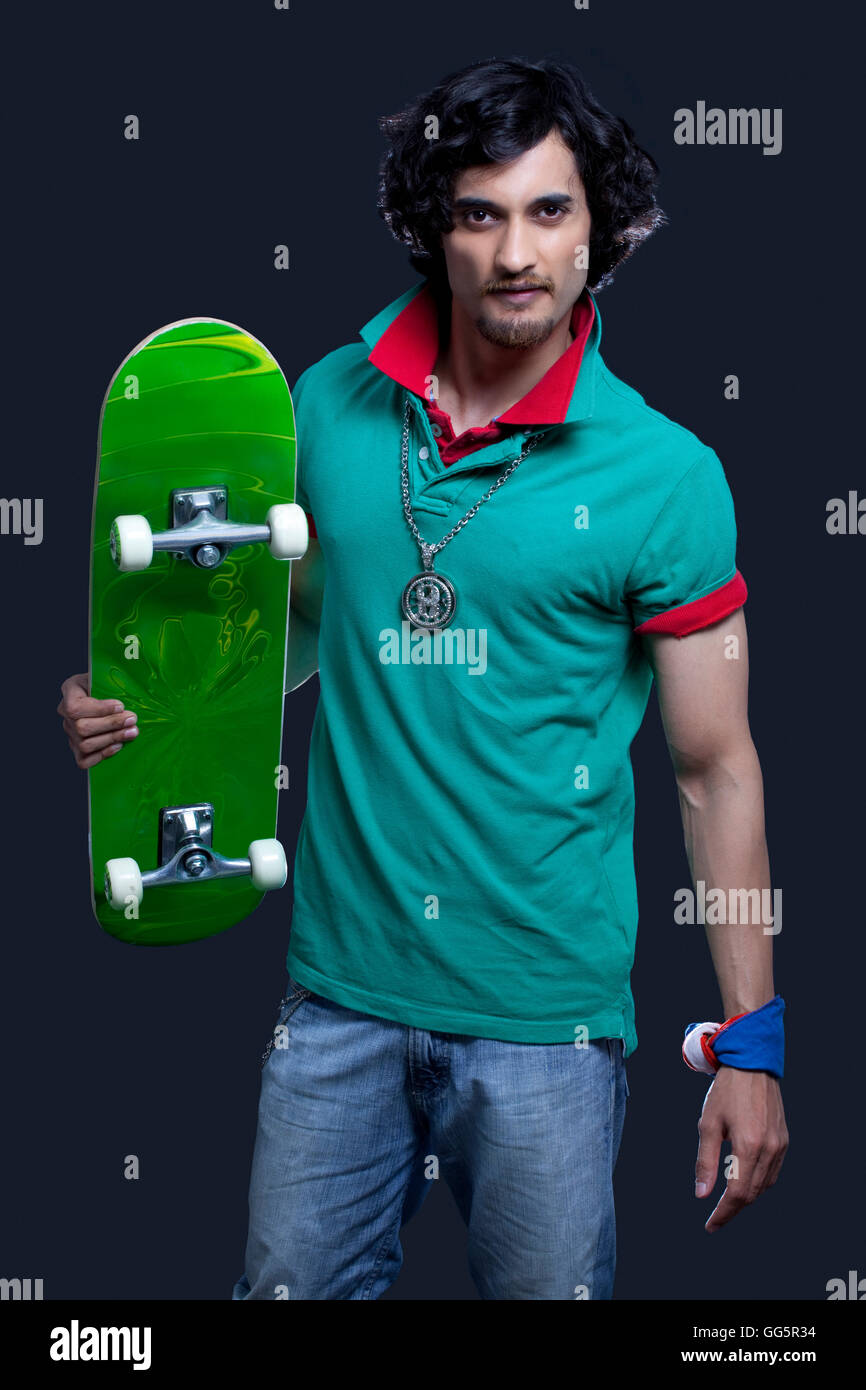 Portrait of a funky young man holding skateboard against black background Stock Photo