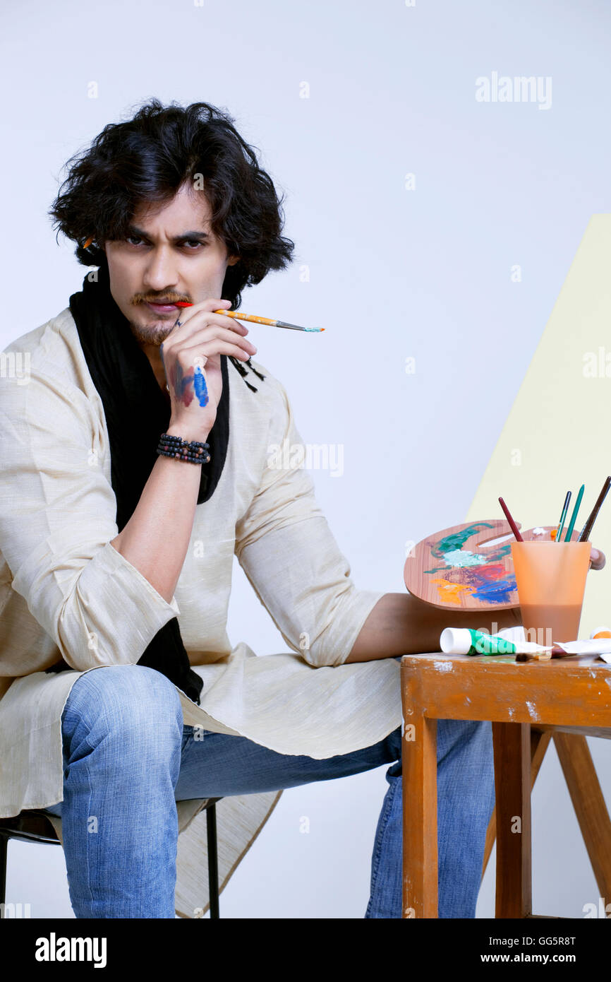 Portrait of handsome male artist with palette and paintbrush against ...