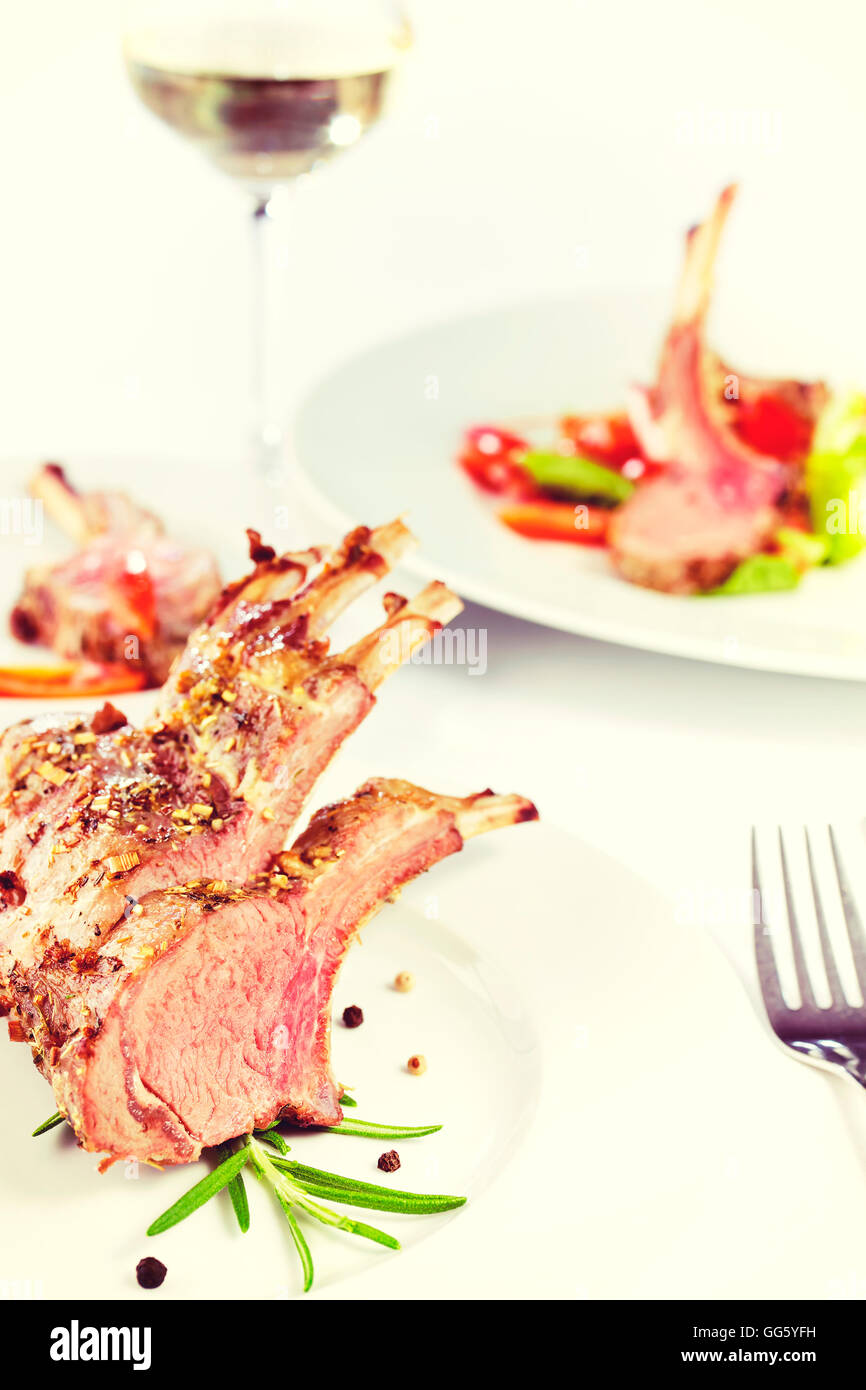 Vintage toned roasted lamb rib chops, dinner setting with white vine. Stock Photo