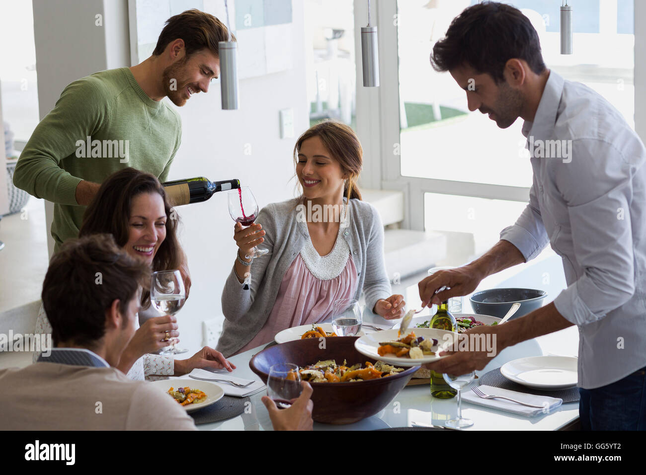 Man serving food to his friends at dining table Stock Photo