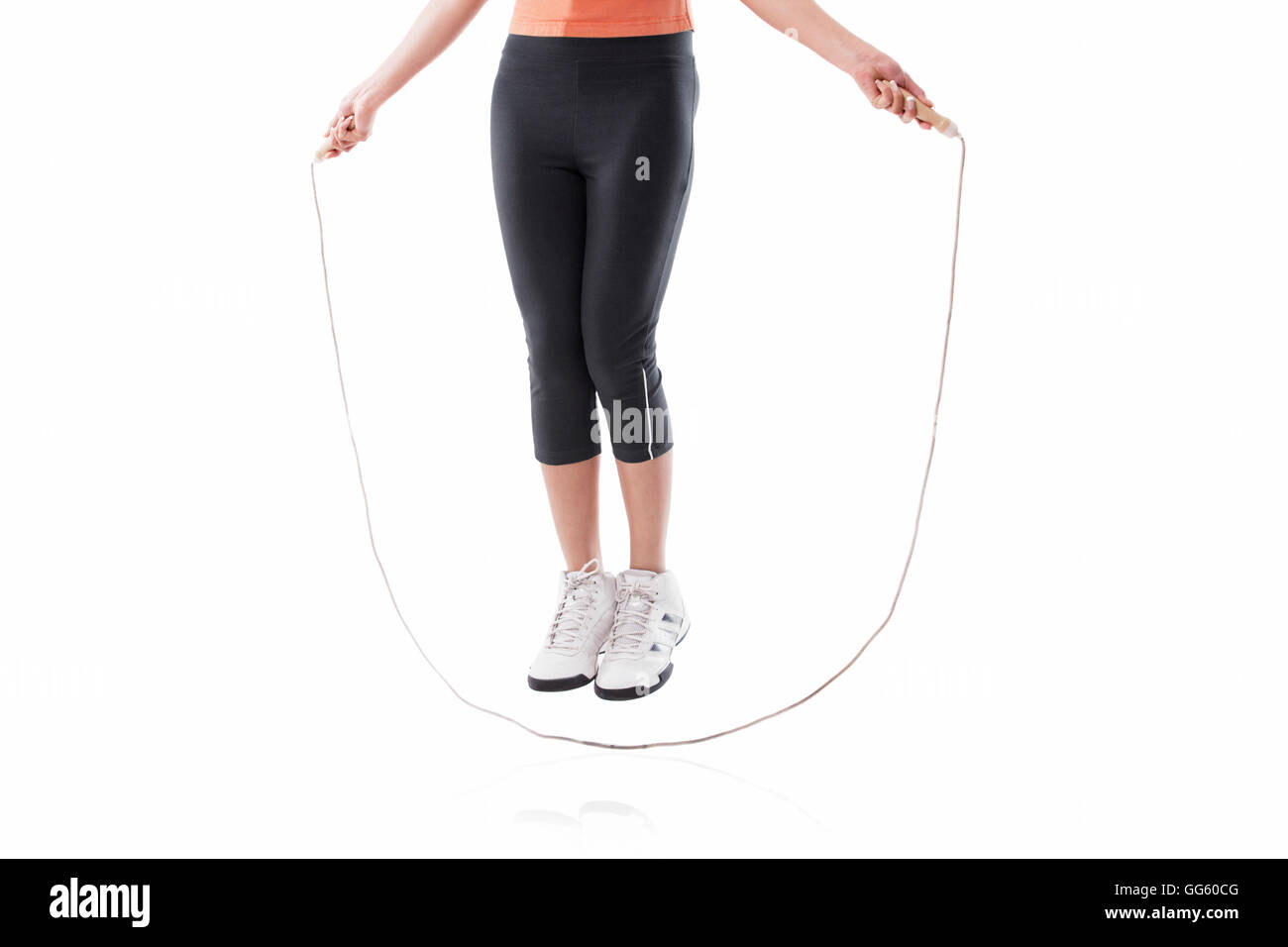 Low section of a woman exercising with jump rope over white background ...