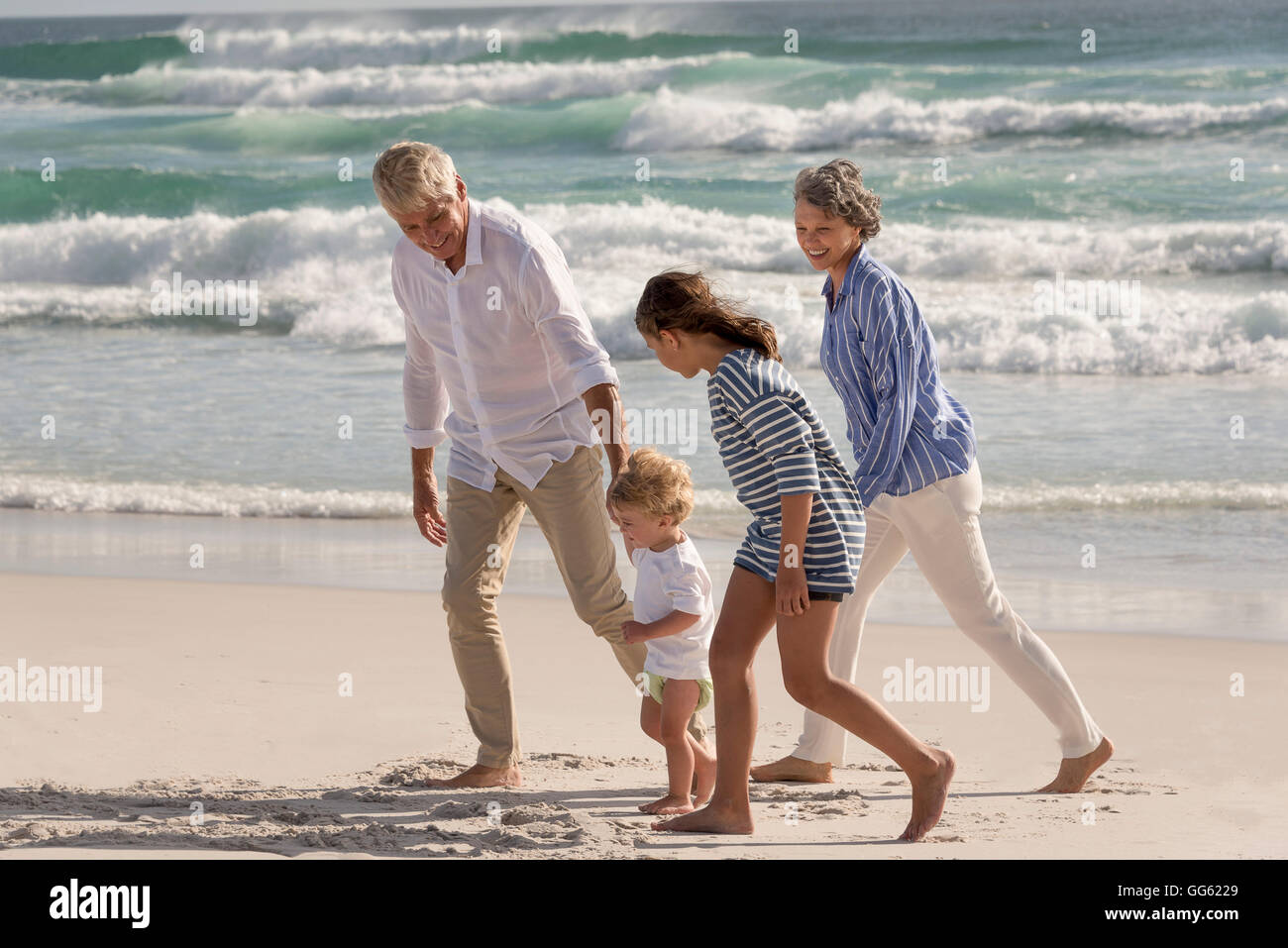 Happy grandparents walking with grandchildren on beach Stock Photo
