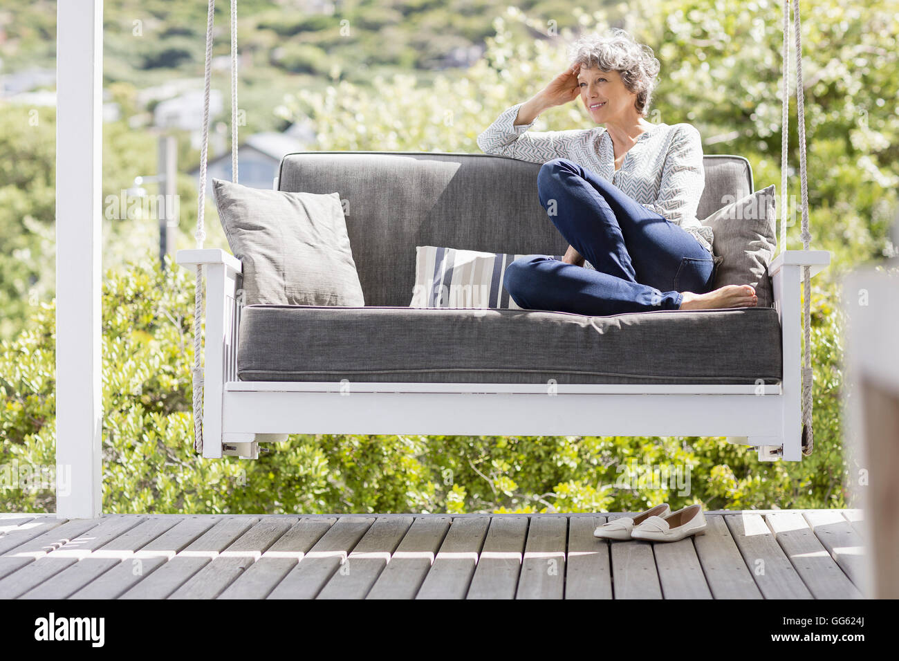 Happy mature woman sitting on a swing in a porch Stock Photo - Alamy