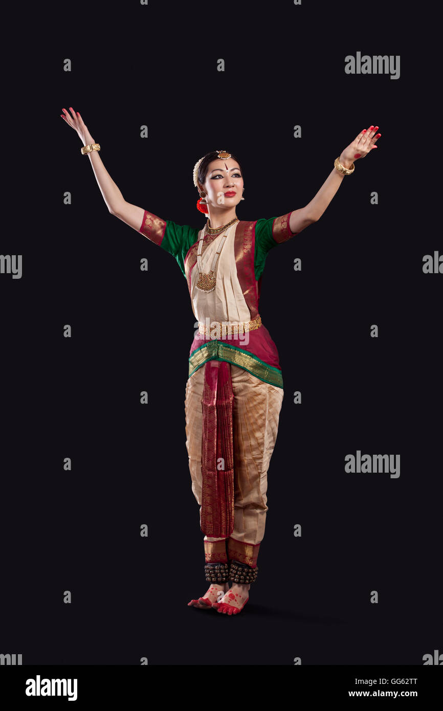 Full length of dancer with arms raised performing Bharatanatyam against black background Stock Photo