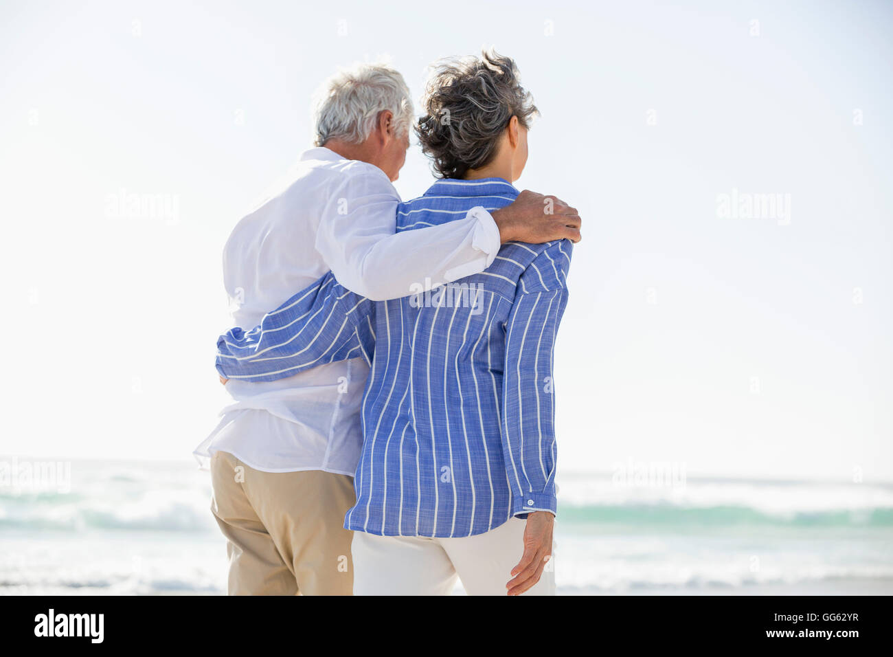 Rear View Of A Couple Standing With Arm Around Each Other On The Beach