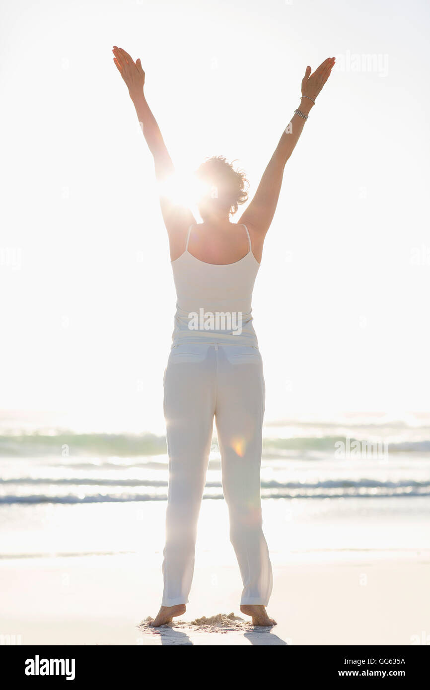 Rear view of a woman standing on the beach with arms raised Stock Photo ...