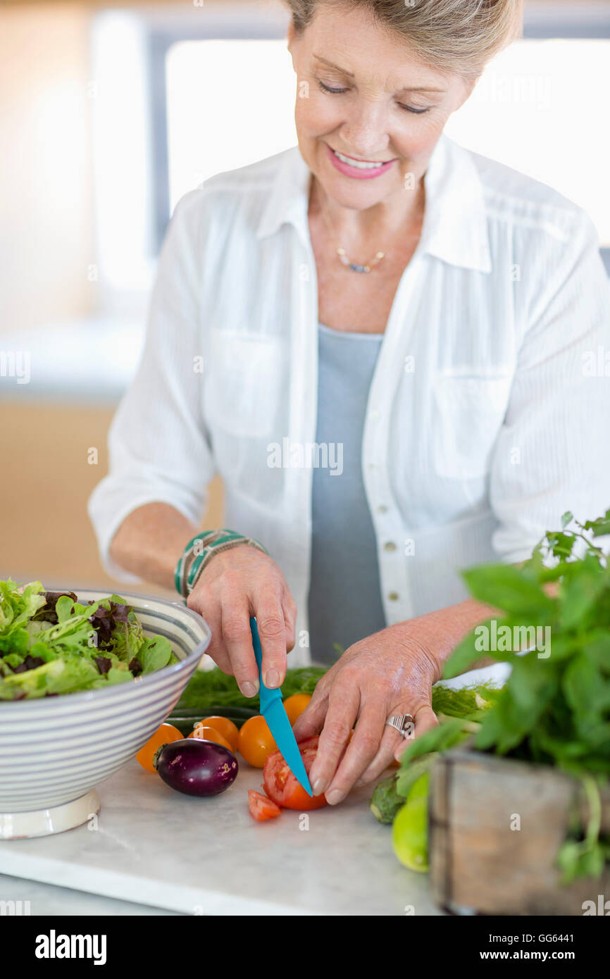 Happy senior woman cutting vegetables in kitchen Stock Photo