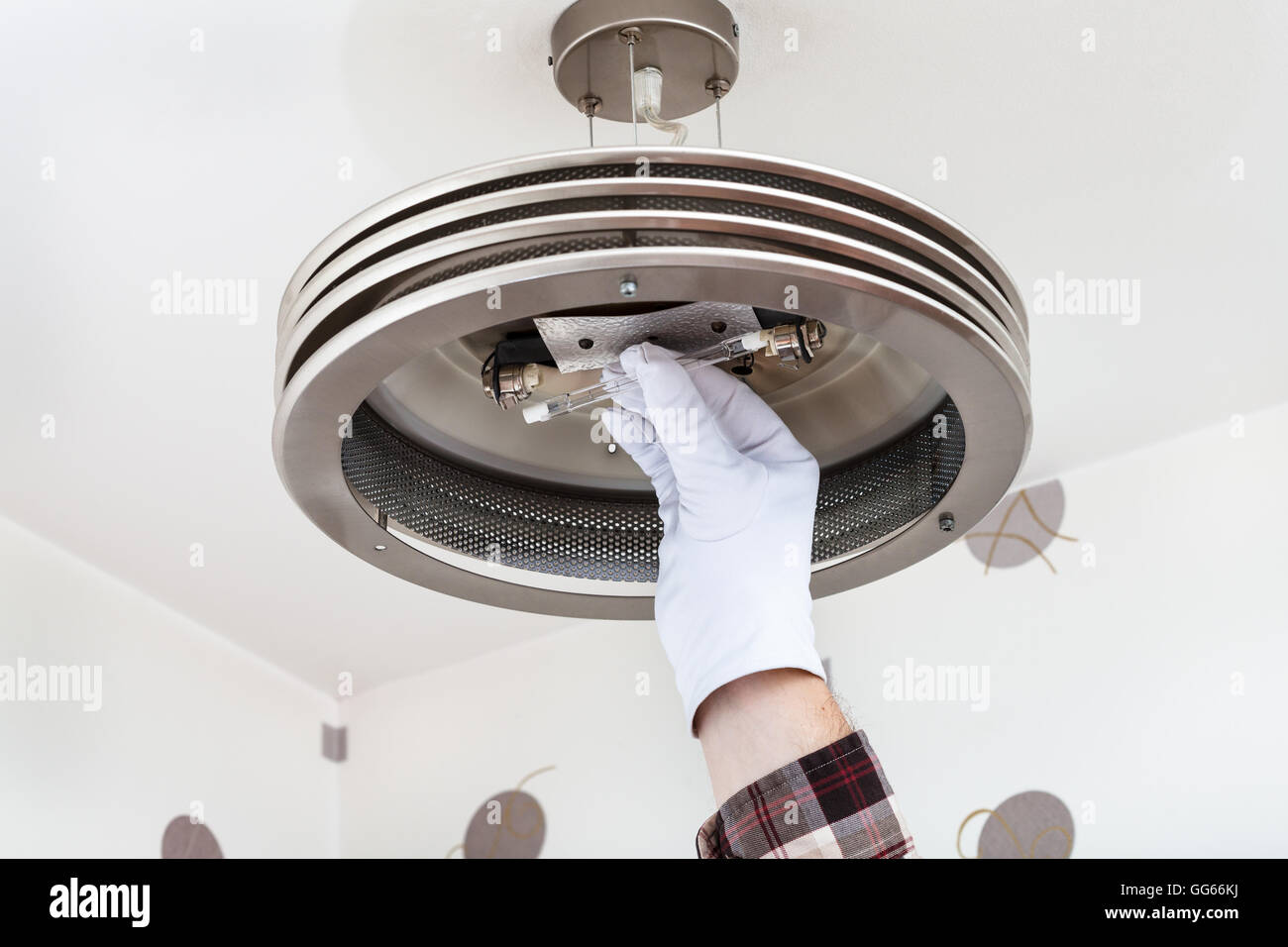 Electrician mounts halogen lamp in ceiling light in room Stock Photo