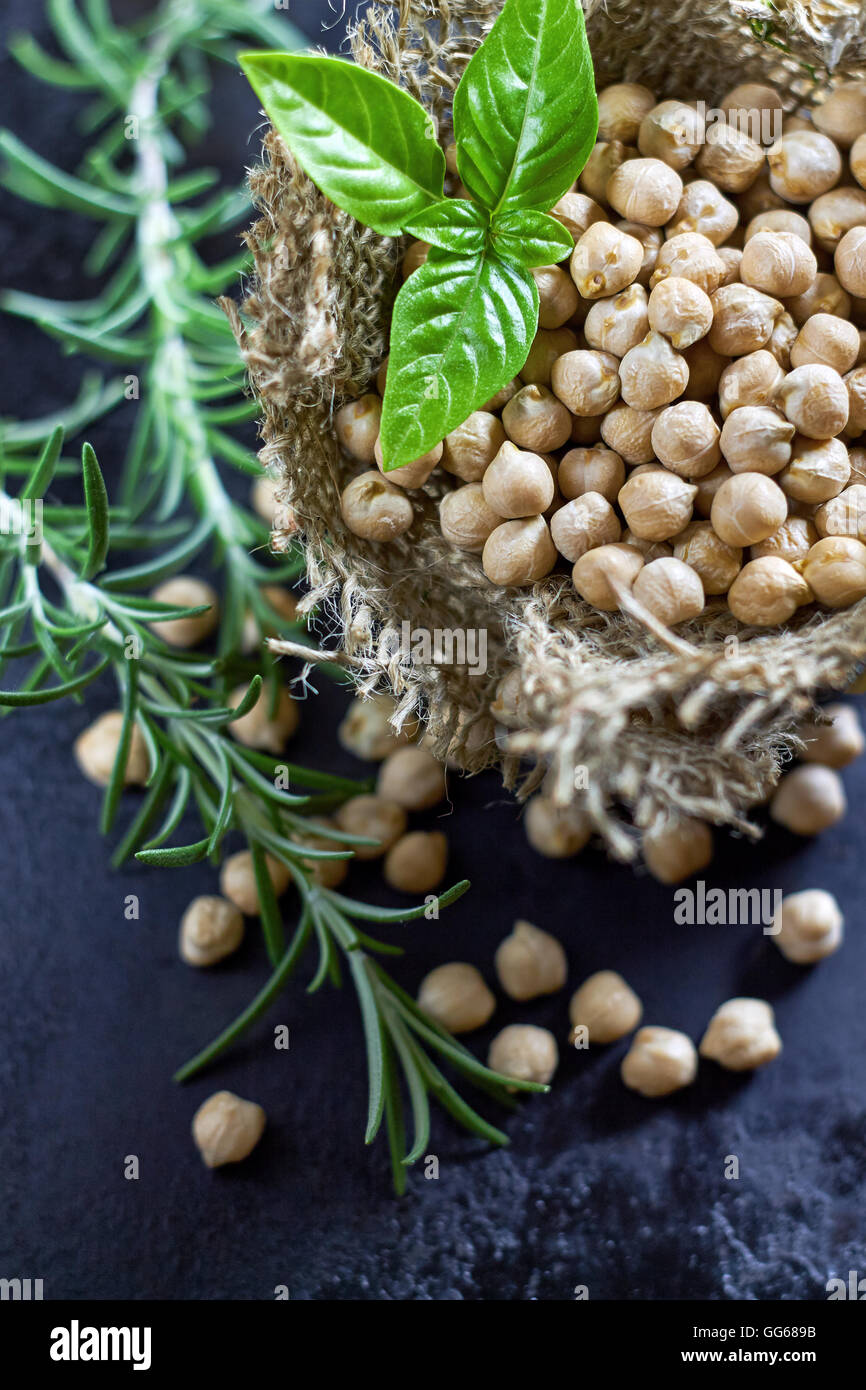 Garbanzo beans (chickpeas) with basil in small burlap bag on black rustic background. Top view Stock Photo