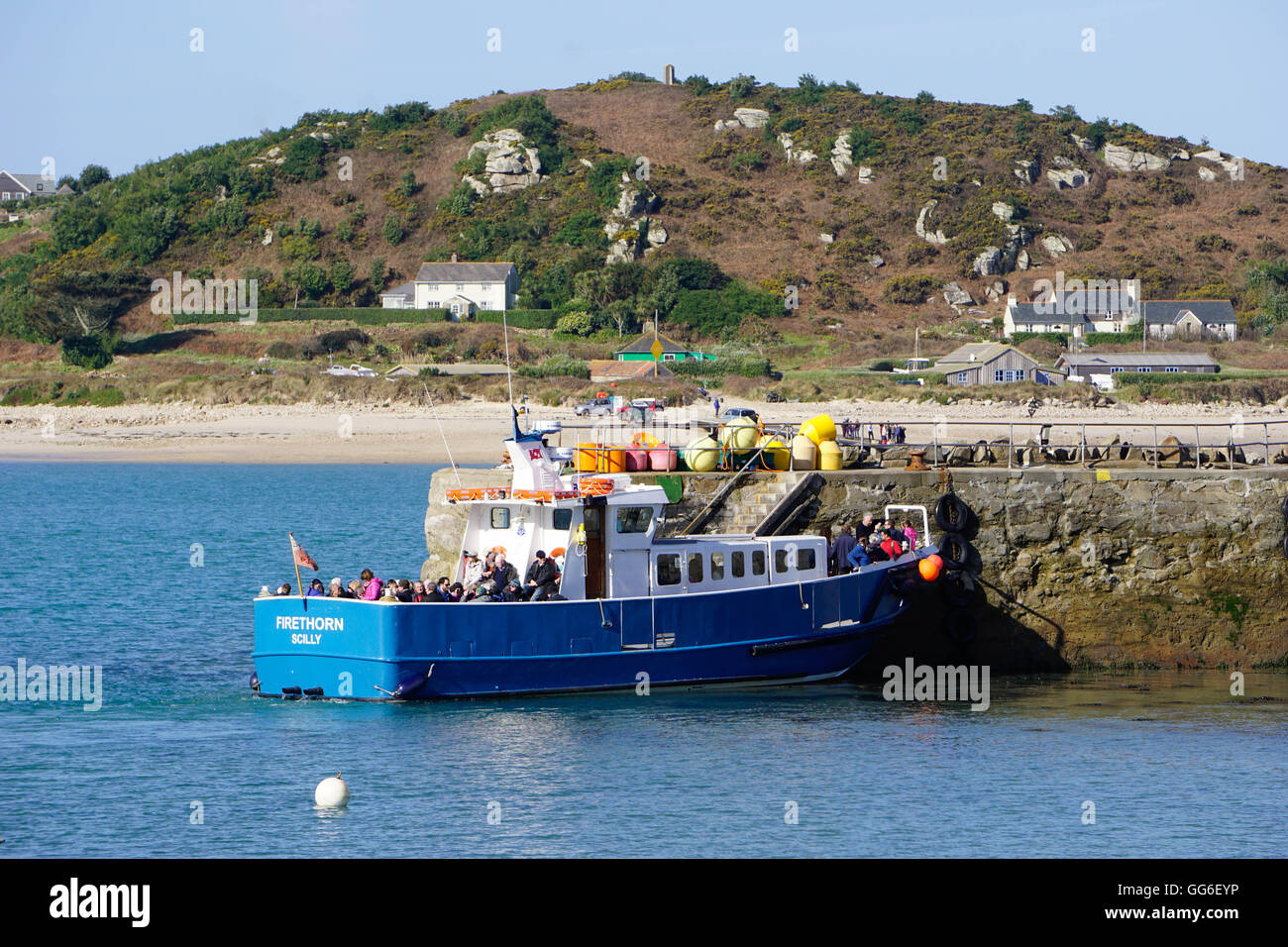 Travellers boarding boat at New Grimsby Quay on Tresco with Bryher in background, Isles of Scilly, England, United Kingdom Stock Photo