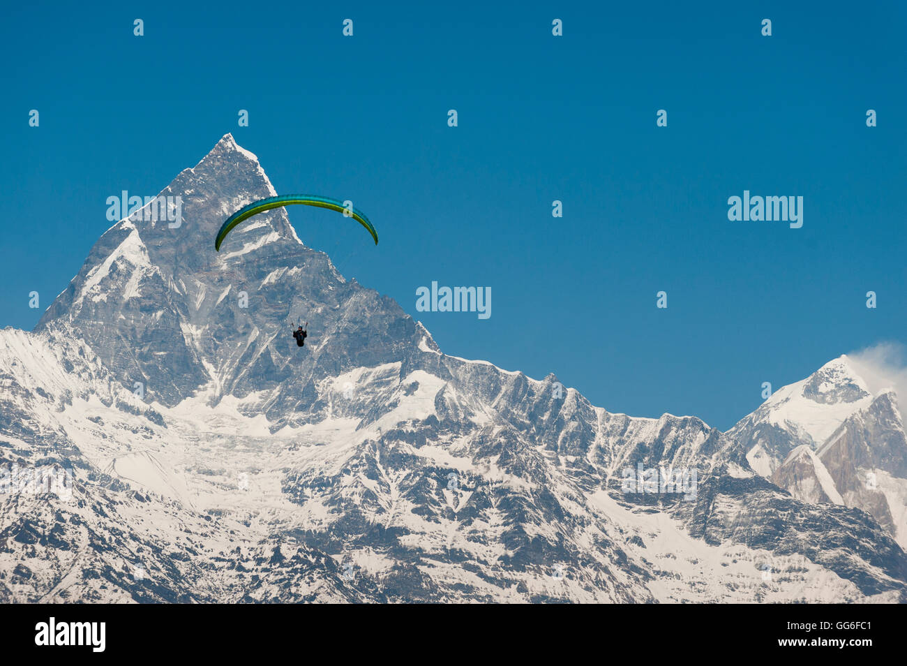 A paraglider hangs in the air with the dramatic peak of Machapuchare (Fishtail mountain) in the distance, Himalayas, Nepal, Asia Stock Photo