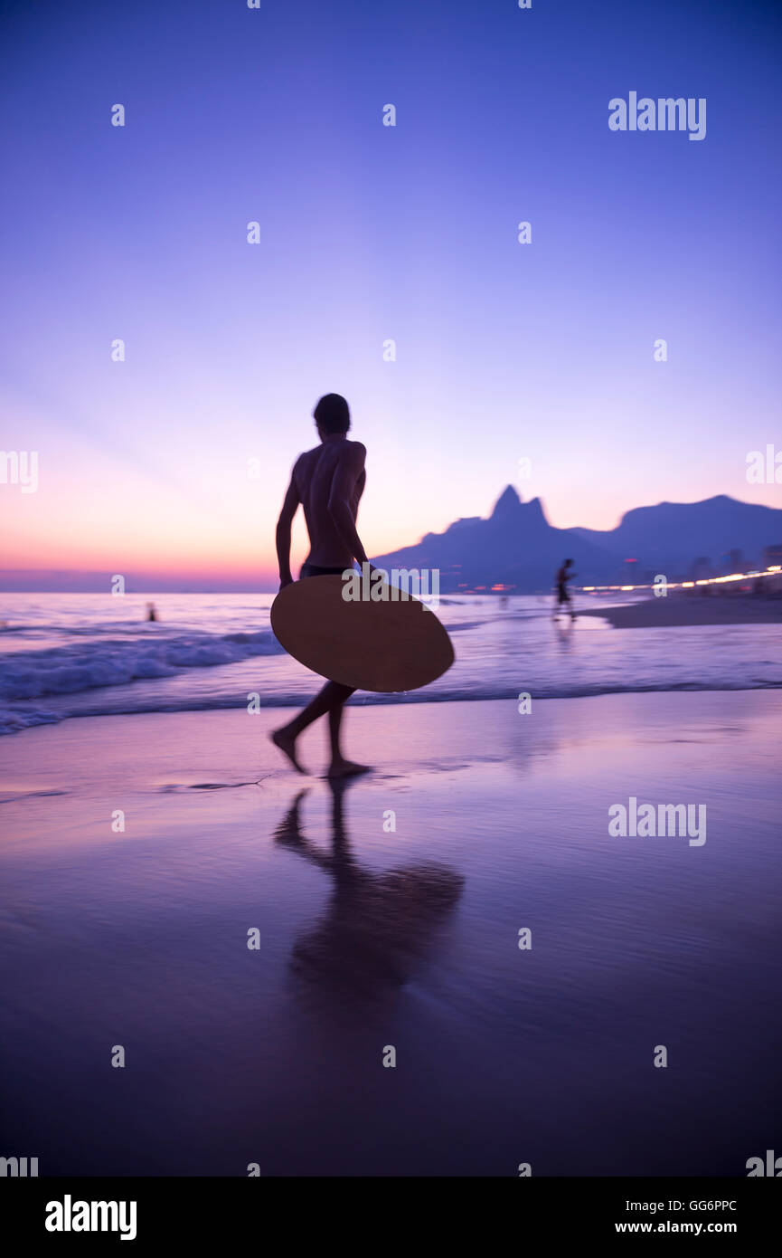 Sunset silhouette of carioca Brazilian running with skimboard on Ipanema Beach Rio de Janeiro, Brazil Stock Photo