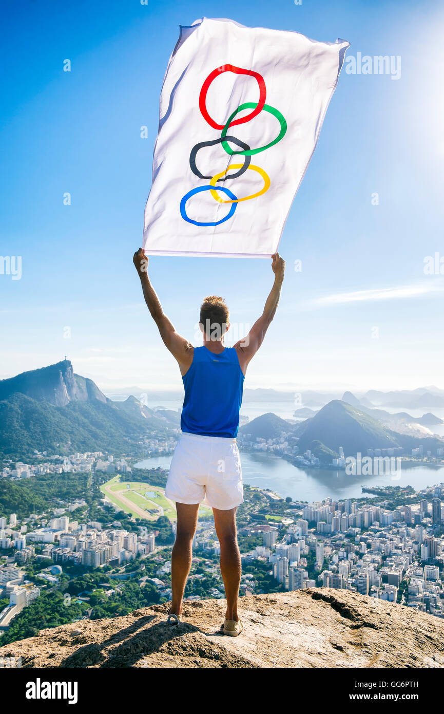 RIO DE JANEIRO - MARCH 21, 2016: Athlete stands holding Olympic flag above a city skyline view of Corcovado Mountain. Stock Photo