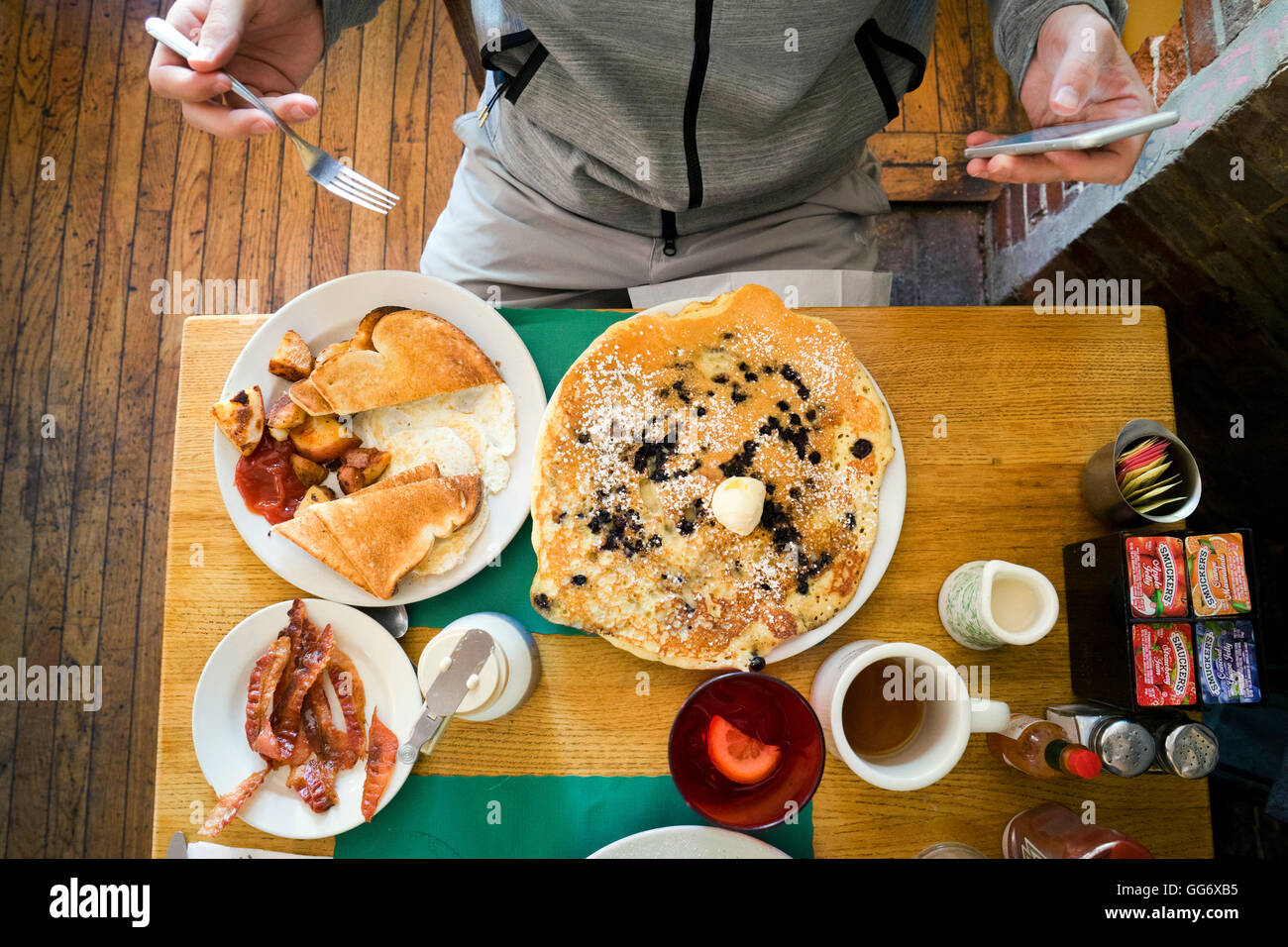 Man sitting in front of breakfast food, using smartphone Stock Photo