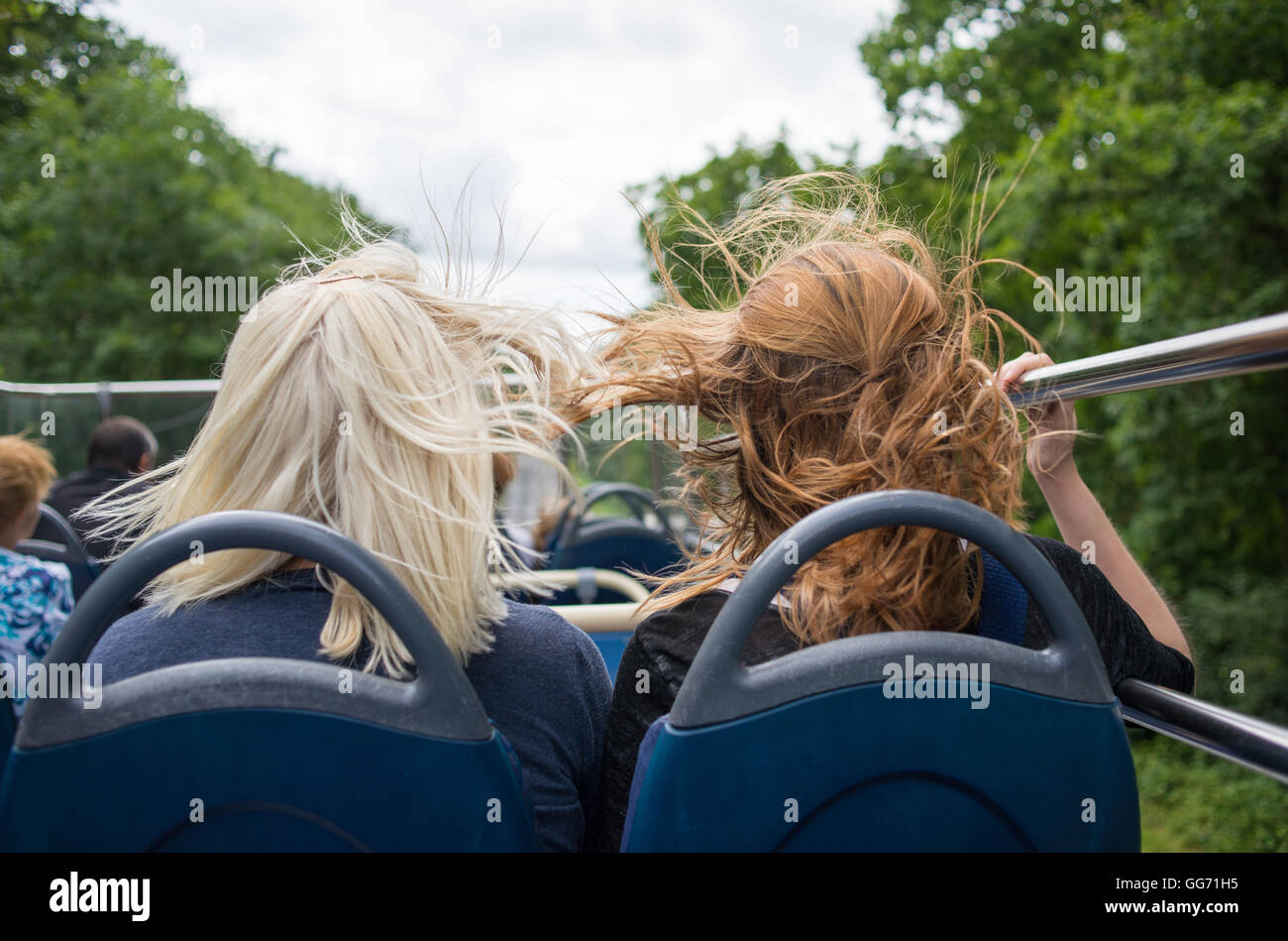 It's windy on the top deck of an open top bus when it's moving as these two women passengers are finding out. Stock Photo