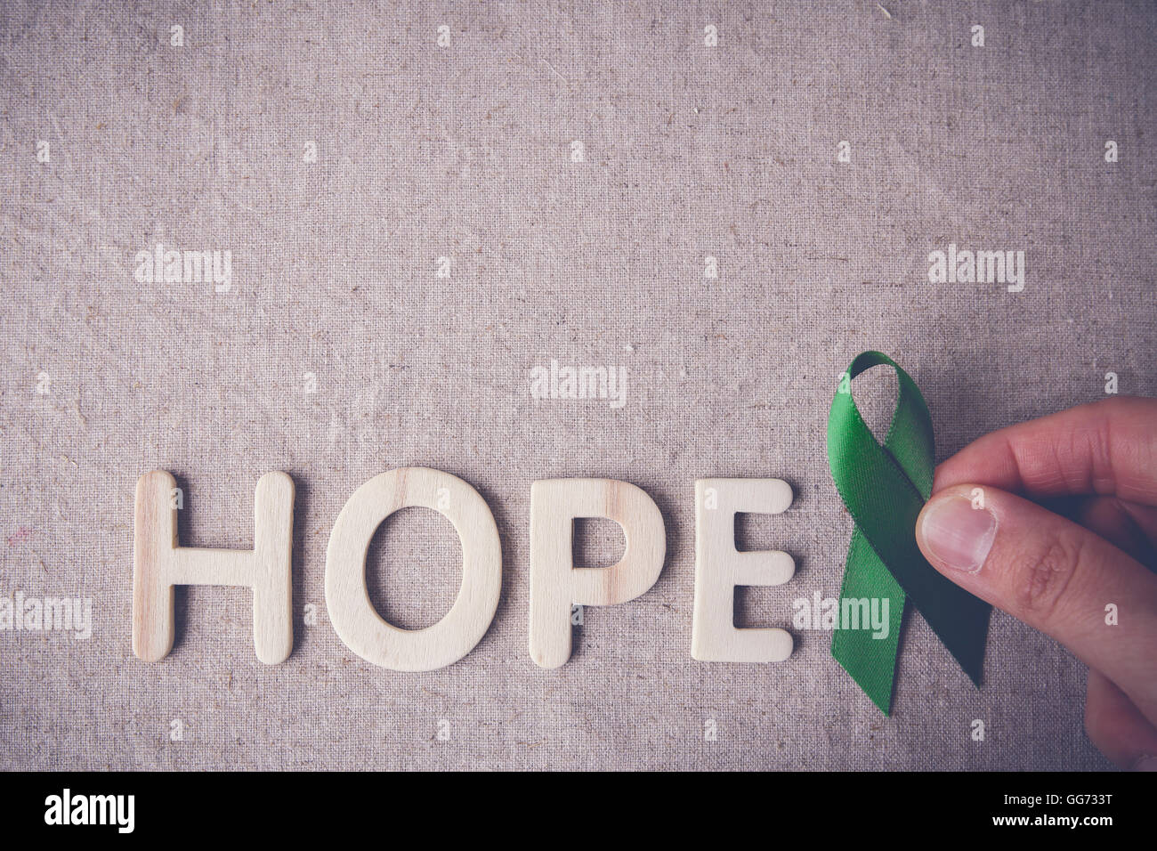 fingers holding Green Ribbon with HOPE wooden word, cancer awareness, Liver, kidney cancer awareness Stock Photo